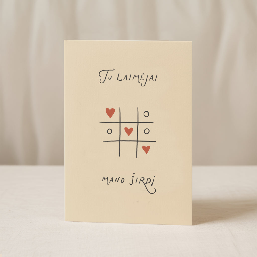 Romantic greeting card featuring a tic-tac-toe game with heart symbols instead of X and O, and the phrase “Tu laimėjai mano širdį” written below.