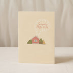 Cozy housewarming greeting card featuring an illustrated cottage with chimney smoke forming the words “Laimingų naujų namų”, warm new home celebration design.