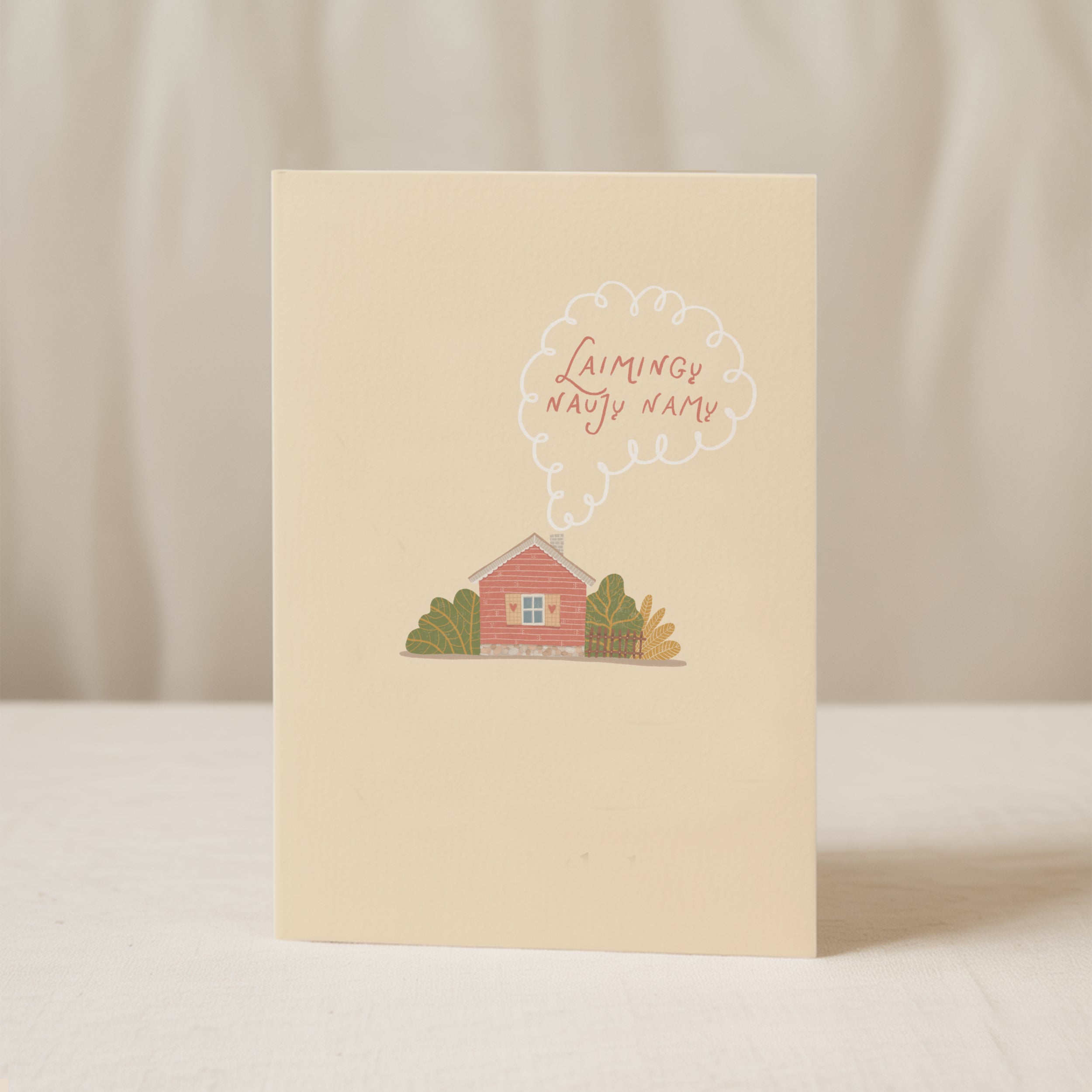 Cozy housewarming greeting card featuring an illustrated cottage with chimney smoke forming the words “Laimingų naujų namų”, warm new home celebration design.