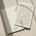 Minimalist birthday greeting card featuring a crossword-style letter puzzle with the hidden message “Sveikinu su gimimo diena” on a white background.