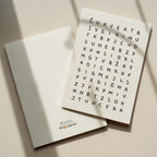 Minimalist birthday greeting card featuring a crossword-style letter puzzle with the hidden message “Sveikinu su gimimo diena” on a white background.