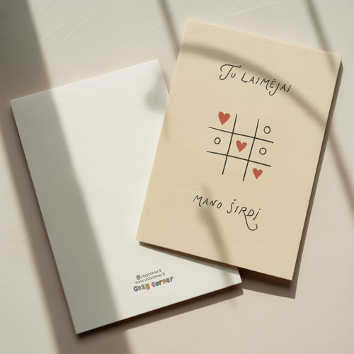 Romantic greeting card featuring a tic-tac-toe game with heart symbols instead of X and O, and the phrase “Tu laimėjai mano širdį” written below.