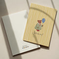 Greeting card featuring a cute teddy bear holding a balloon with the word “SVEIKINU!” on a yellow striped background, cheerful celebration card design.