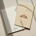 Cozy housewarming greeting card featuring an illustrated cottage with chimney smoke forming the words “Laimingų naujų namų”, warm new home celebration design.
