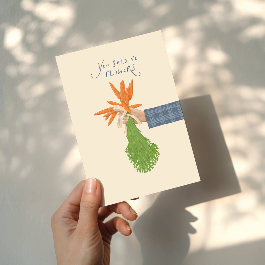 Funny wedding greeting card showing a hand holding a bouquet of carrots instead of flowers with the text “You said no flowers”, humorous minimalist wedding design.