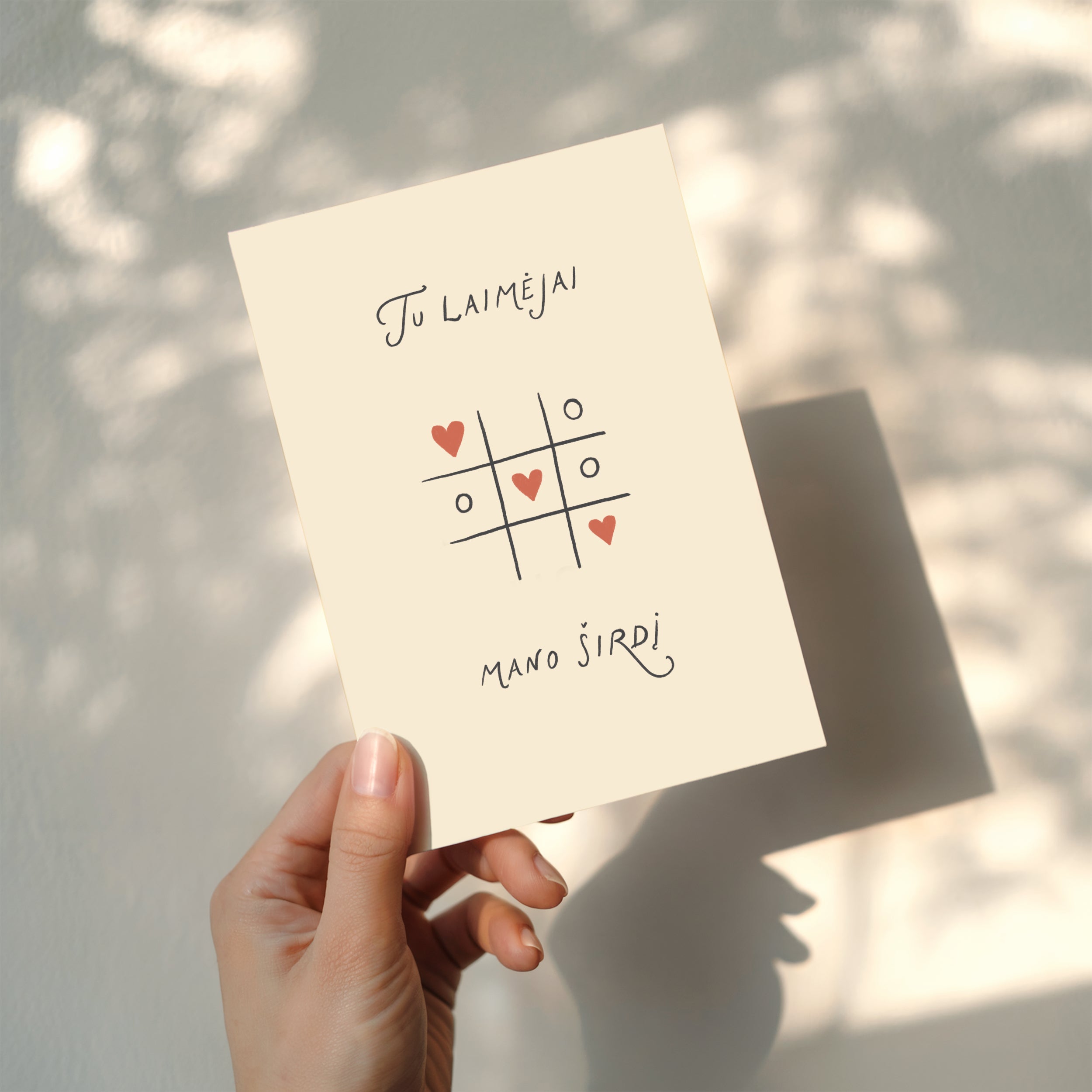 Romantic greeting card featuring a tic-tac-toe game with heart symbols instead of X and O, and the phrase “Tu laimėjai mano širdį” written below.