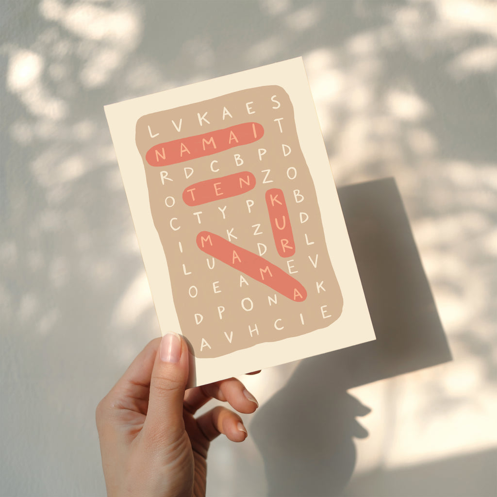 Minimalist greeting card featuring a letter puzzle crossword design with highlighted words “Namai ten kur mama” on a clean white background.