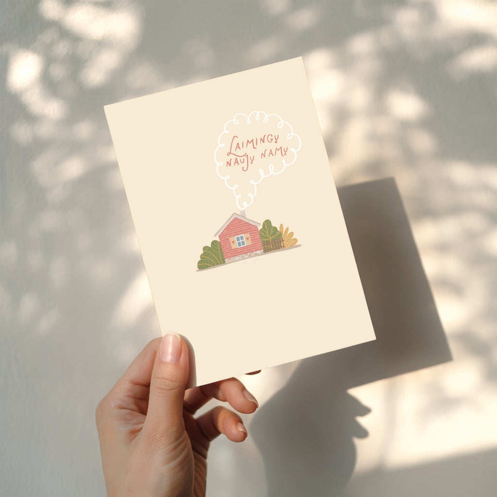 Cozy housewarming greeting card featuring an illustrated cottage with chimney smoke forming the words “Laimingų naujų namų”, warm new home celebration design.
