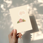 Cozy housewarming greeting card featuring an illustrated cottage with chimney smoke forming the words “Laimingų naujų namų”, warm new home celebration design.